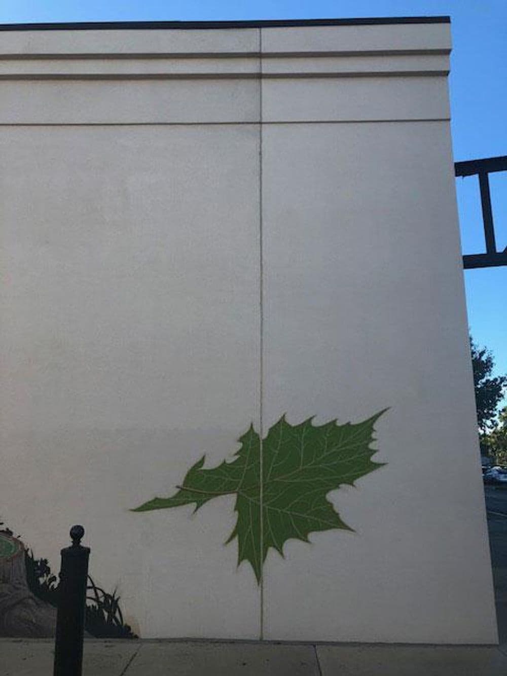 Green leaf mural on a beige wall, adding a touch of nature to the urban setting.