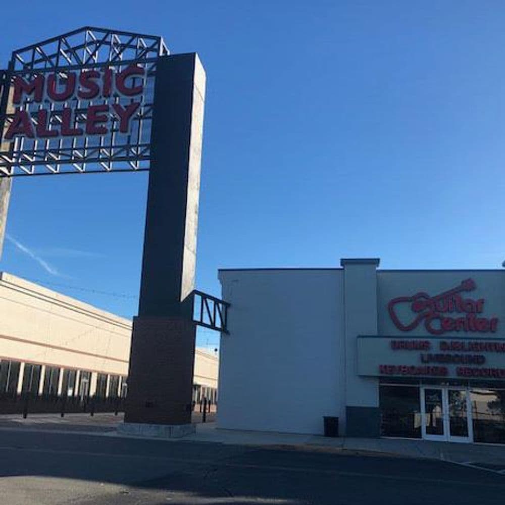 Music Alley sign and Guitar Center storefront under clear blue sky.