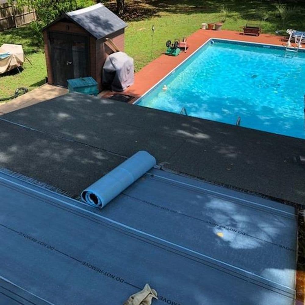 Roofing material being installed next to a pool in a backyard with a shed and outdoor furniture.