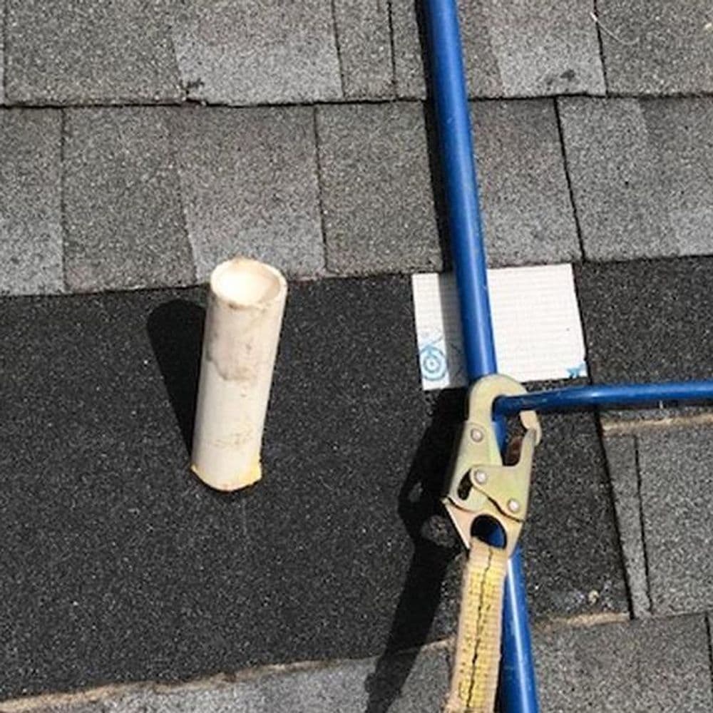 Roofing tools on a shingle surface, including a blue rod, PVC pipe, and clamp.