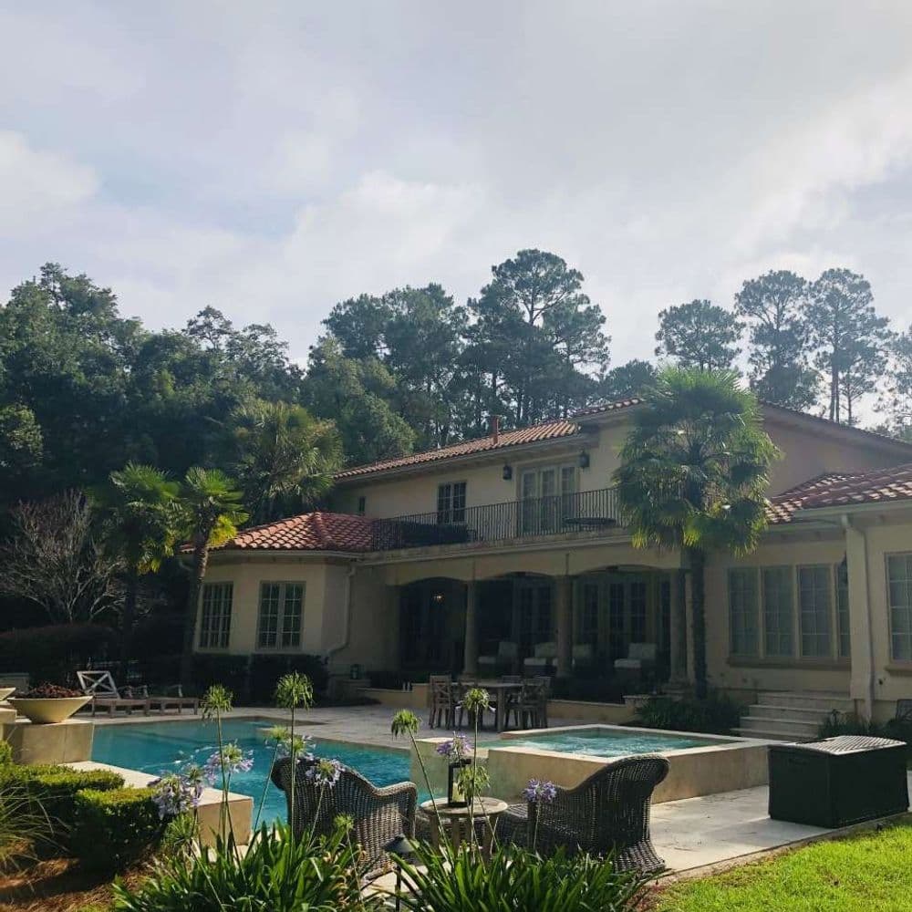 Elegant home with a pool surrounded by lush greenery and patio seating. Ideal for relaxation.
