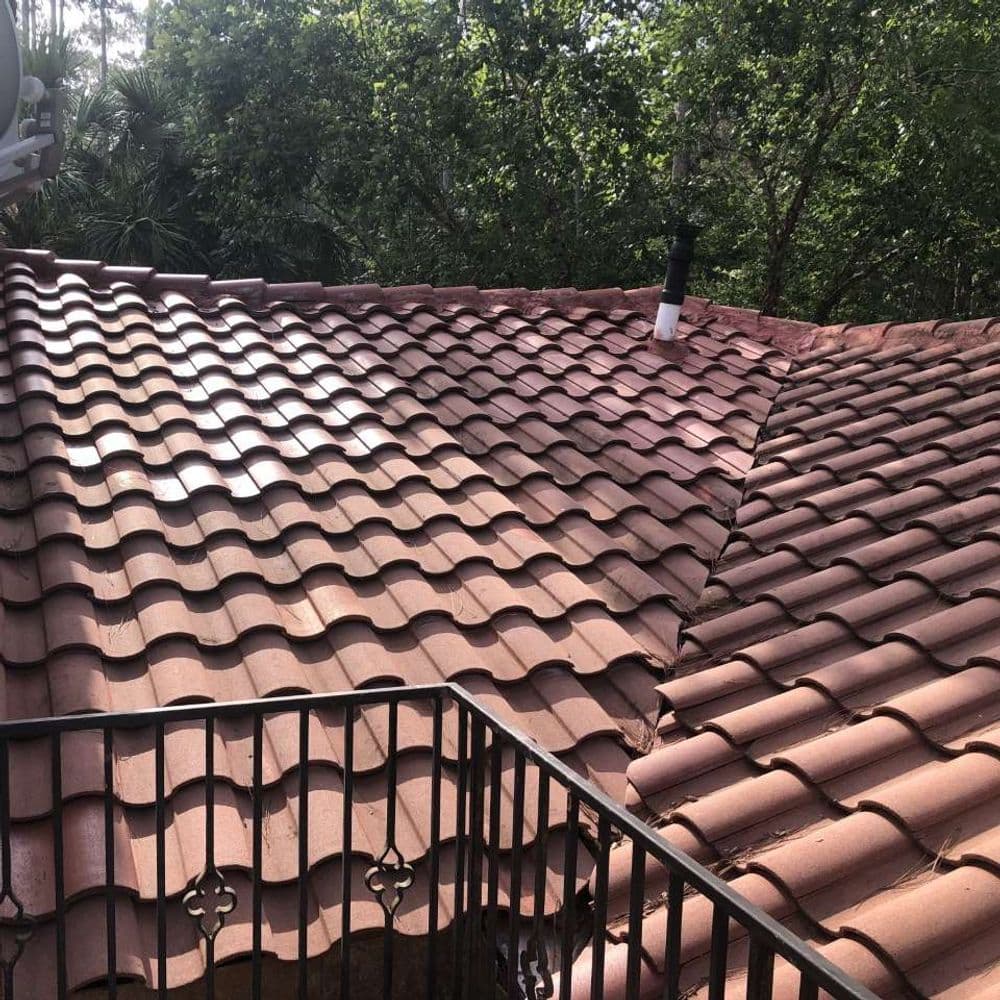 Tile roof with wavy pattern surrounded by greenery, showcasing a chimney and balcony view.