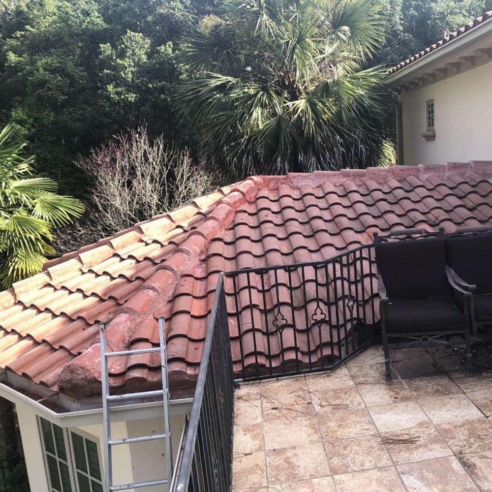 Roof with terracotta tiles, surrounded by greenery and a balcony with chairs.