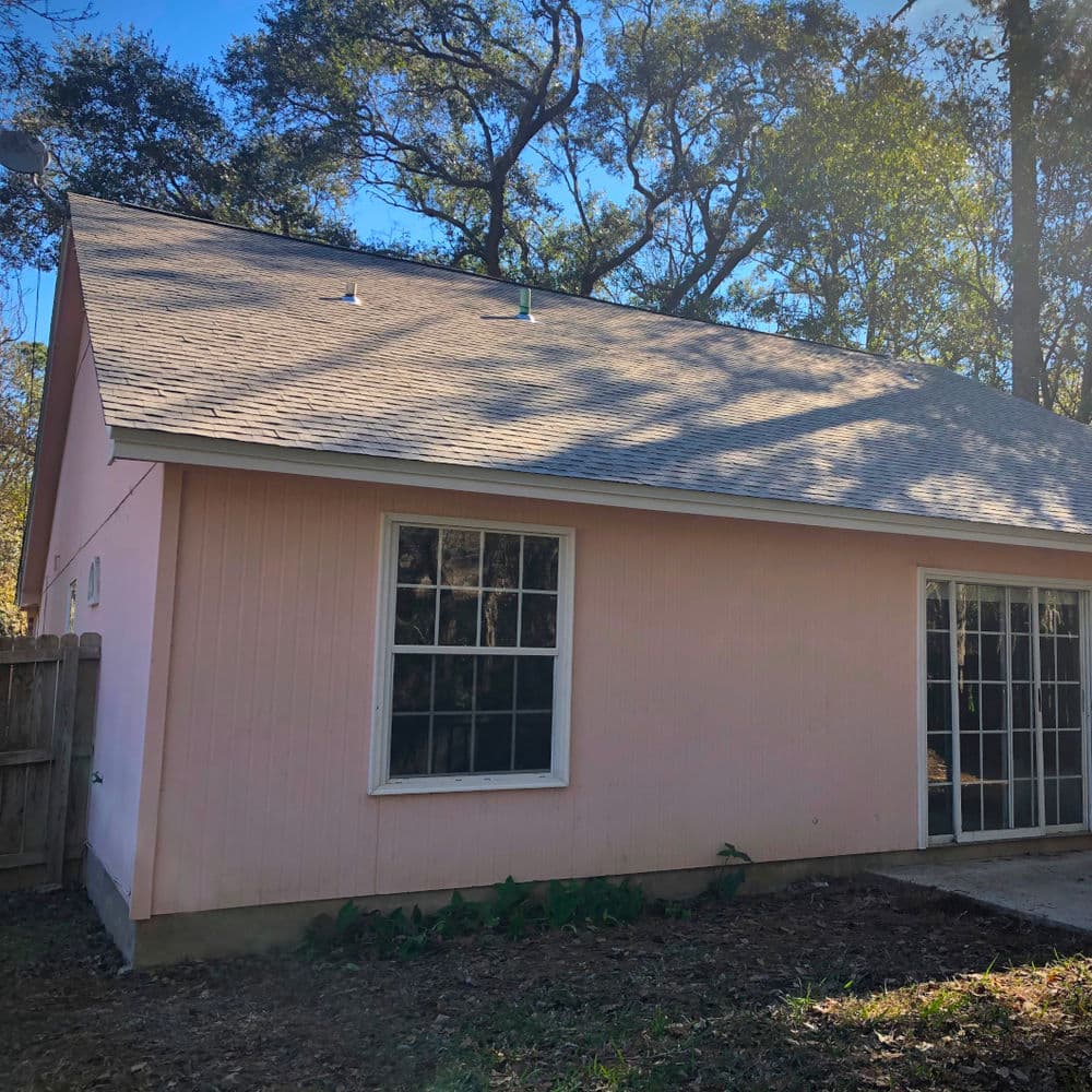 Pink exterior of a house surrounded by trees, featuring large windows and a backyard.