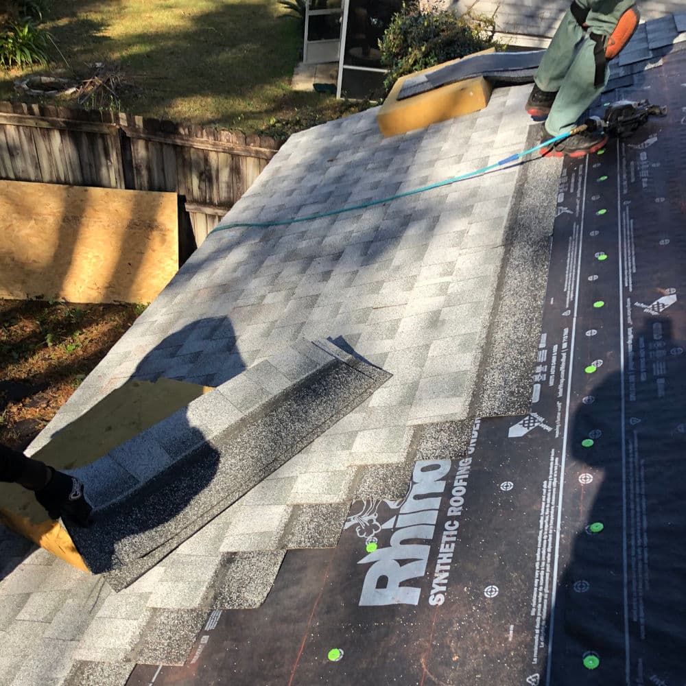 Workers installing synthetic roofing shingles on a residential roof.
