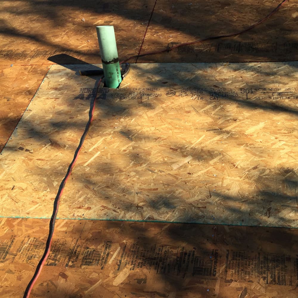 Construction site featuring outdoor plywood flooring with a green pipe and electrical cord.