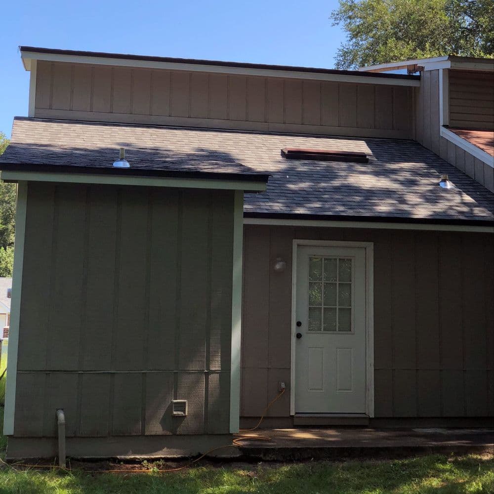 Contemporary house exterior with a sloped roof, green siding, and a small front door.