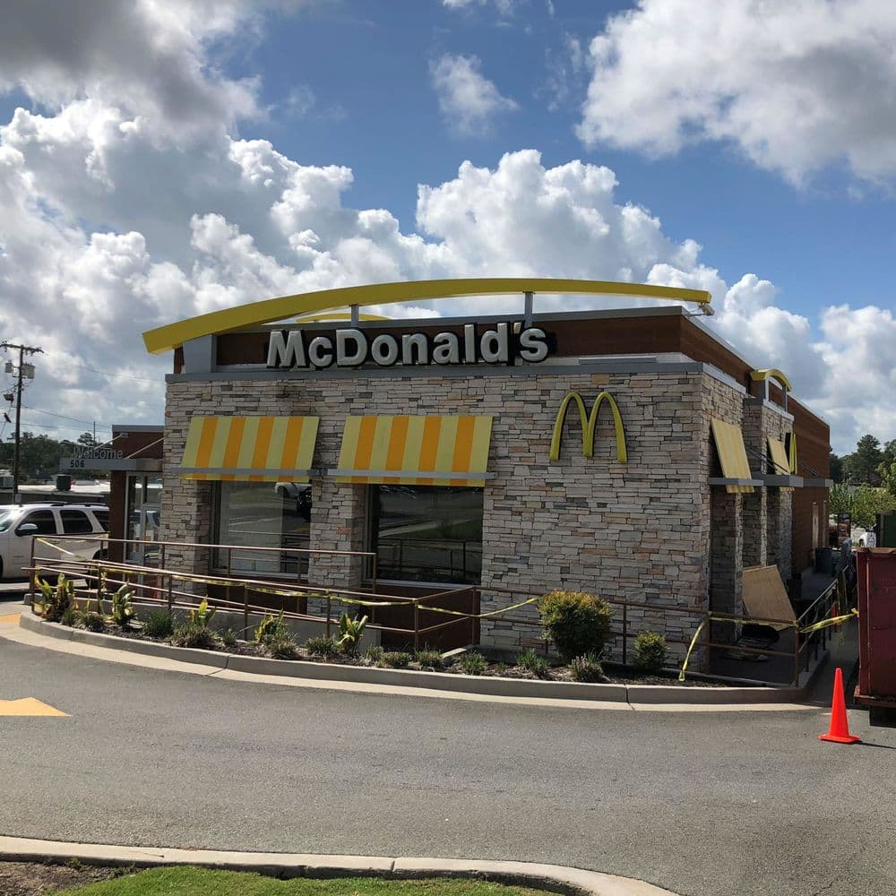McDonald's restaurant exterior with yellow awnings and stone facade under a cloudy sky.