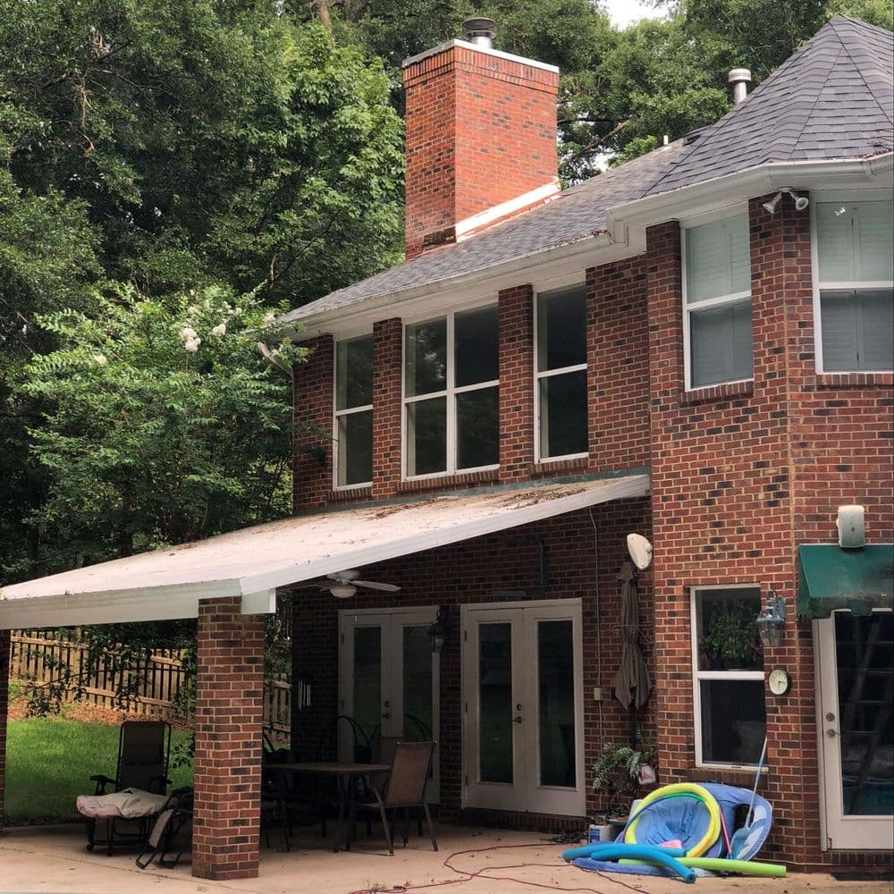 Brick house exterior with a covered patio, chimney, and a lush green backyard.